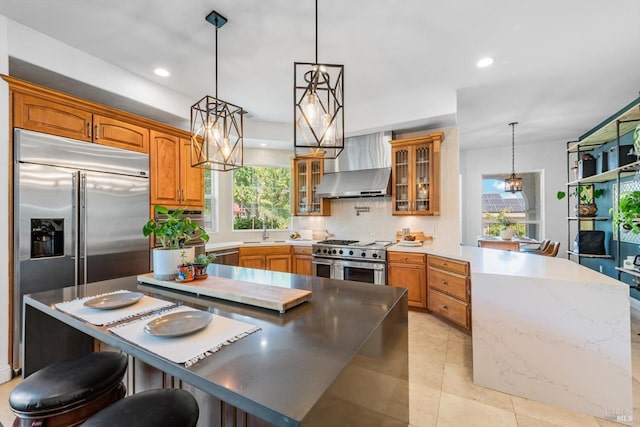 kitchen featuring premium appliances, a sink, wall chimney range hood, a peninsula, and decorative backsplash