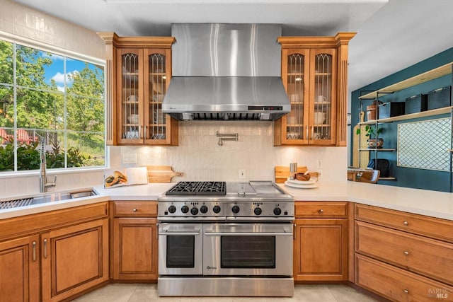kitchen featuring light countertops, brown cabinets, wall chimney range hood, and double oven range