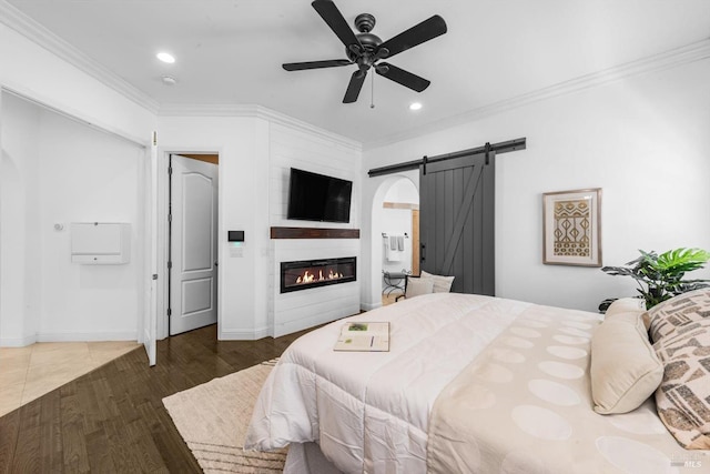 bedroom featuring a barn door, recessed lighting, wood finished floors, ornamental molding, and a large fireplace