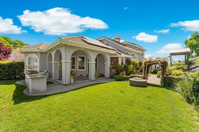 back of property with roof mounted solar panels, a tile roof, a lawn, and stucco siding