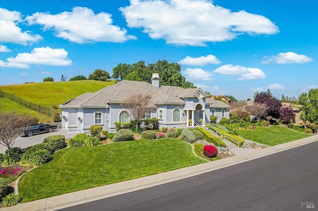 view of front of house featuring a front yard, a chimney, concrete driveway, a tile roof, and stucco siding