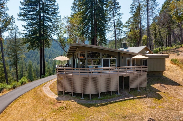 back of property featuring crawl space, a view of trees, a wooden deck, and a lawn