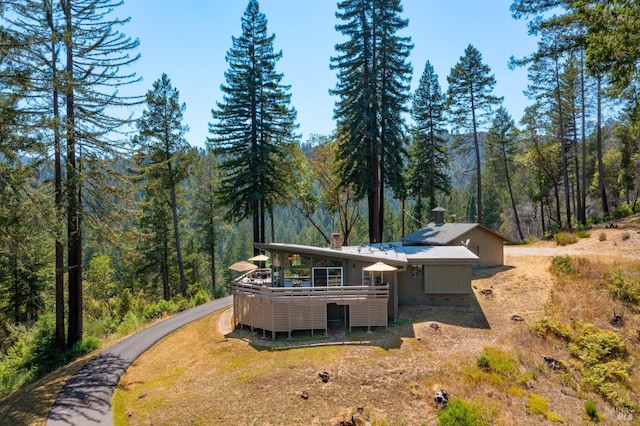 back of house with a forest view, a chimney, and a wooden deck
