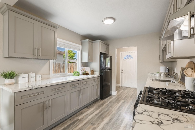 kitchen featuring a sink, black appliances, light wood-style floors, under cabinet range hood, and gray cabinetry