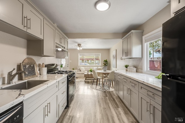 kitchen featuring light wood-type flooring, gray cabinets, black appliances, under cabinet range hood, and a sink