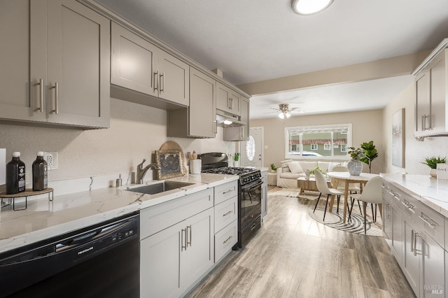 kitchen featuring light wood-type flooring, light stone counters, black appliances, gray cabinetry, and a sink