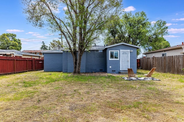 back of property with a yard, a fenced backyard, an outdoor fire pit, and stucco siding