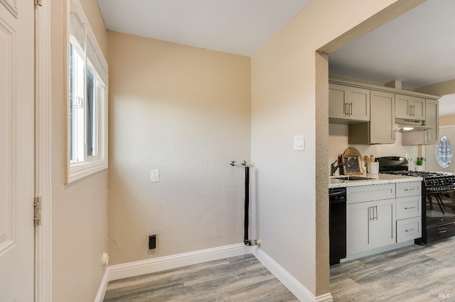 kitchen featuring a sink, light wood-style floors, light countertops, under cabinet range hood, and black appliances