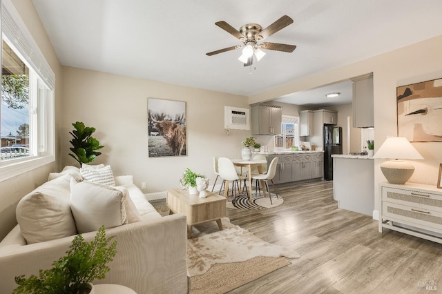 living area with a ceiling fan, light wood-style floors, and a wall mounted air conditioner
