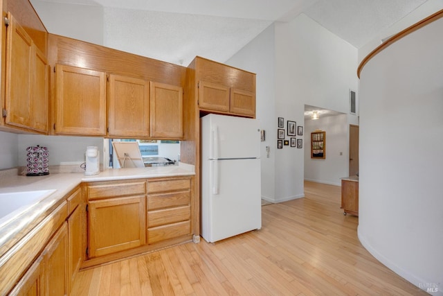 kitchen featuring high vaulted ceiling, light wood finished floors, light countertops, and freestanding refrigerator