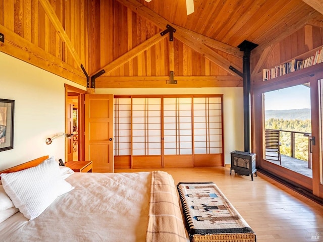 bedroom with a wood stove, wood ceiling, wood finished floors, high vaulted ceiling, and access to outside