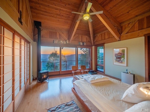 bedroom with a wood stove, wood ceiling, beamed ceiling, wood finished floors, and high vaulted ceiling