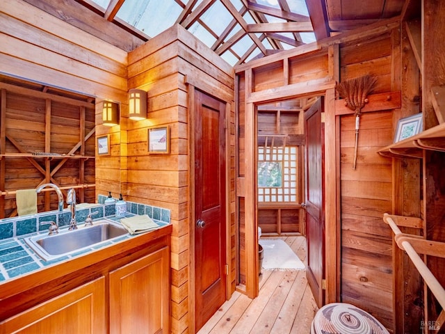 interior space with a sink, tile counters, brown cabinetry, vaulted ceiling, and wood walls