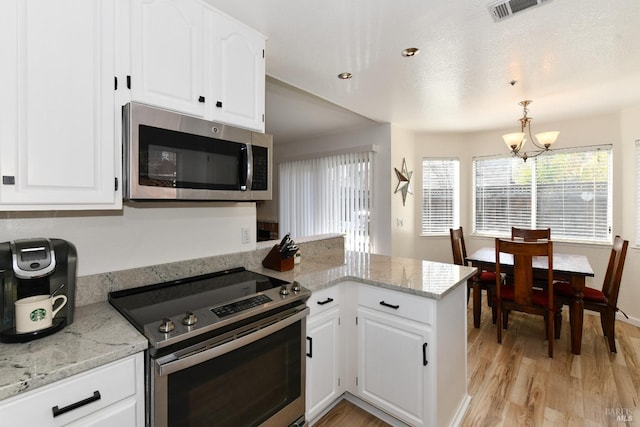 kitchen with light wood-style flooring, a peninsula, white cabinets, stainless steel appliances, and a notable chandelier