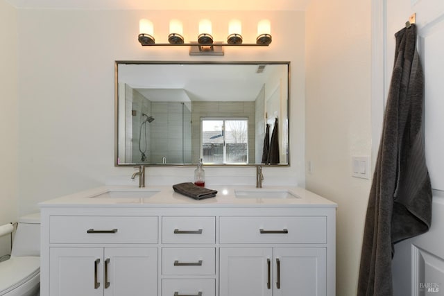 full bath with a sink, toilet, tiled shower, and double vanity