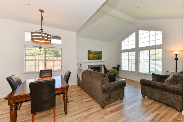 living room with light wood-style floors, high vaulted ceiling, beamed ceiling, a glass covered fireplace, and baseboards