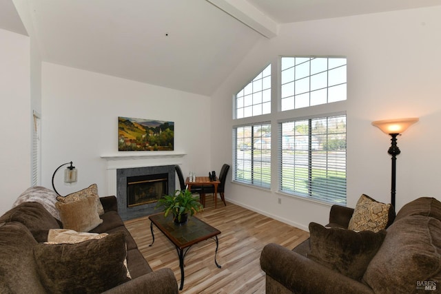living area with light wood-type flooring, baseboards, a fireplace with flush hearth, beam ceiling, and high vaulted ceiling