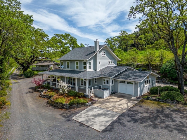 country-style home featuring concrete driveway, roof with shingles, a chimney, an attached garage, and covered porch