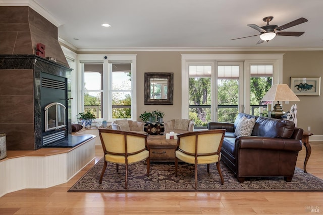 sitting room with wood finished floors, ceiling fan, a tiled fireplace, and ornamental molding