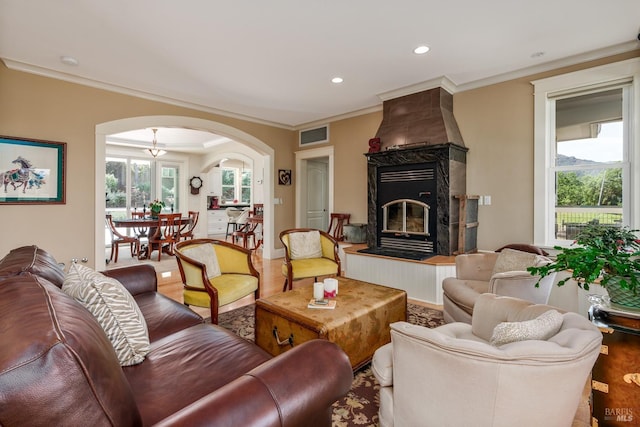 living area with arched walkways, visible vents, crown molding, and wood finished floors