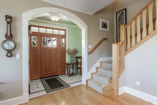 foyer with crown molding, arched walkways, stairway, wood finished floors, and baseboards