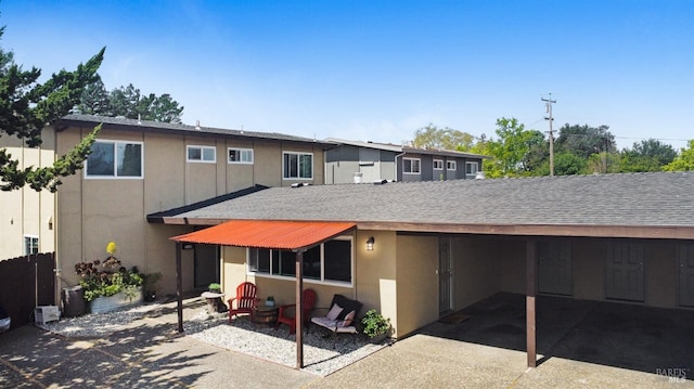 rear view of property with a carport, stucco siding, and a shingled roof