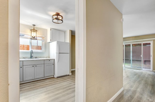 kitchen featuring pendant lighting, freestanding refrigerator, a sink, light countertops, and light wood finished floors