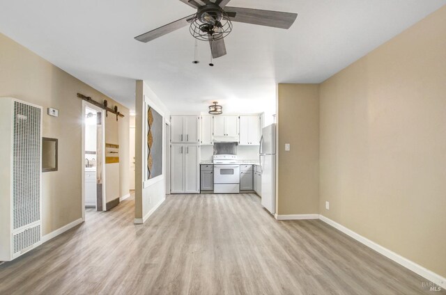 unfurnished living room featuring baseboards, a barn door, a ceiling fan, light wood-style flooring, and a heating unit