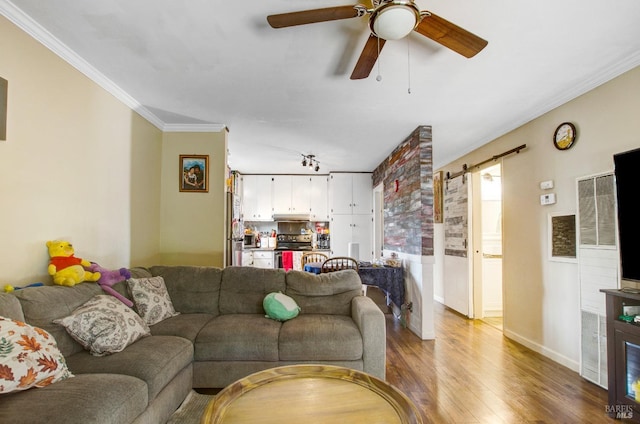 living room with baseboards, a barn door, a ceiling fan, crown molding, and wood finished floors