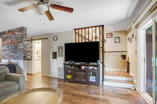 living room featuring a ceiling fan, a barn door, wood finished floors, stairs, and baseboards