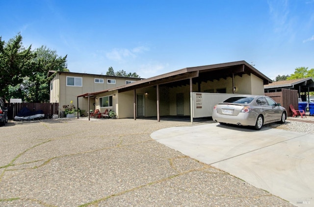 view of front of house with a carport, driveway, fence, and stucco siding