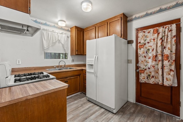 26228 Otter Dr, Willits, CA 95490 - kitchen with gas range oven, white fridge with ice dispenser, under cabinet range hood, brown cabinetry, and a sink