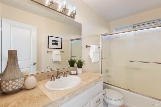 bathroom with bath / shower combo with glass door, vanity, and toilet