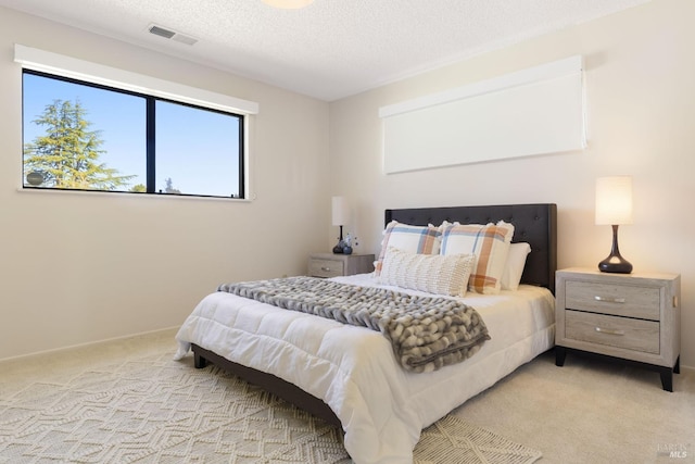 bedroom with baseboards, visible vents, light colored carpet, and a textured ceiling