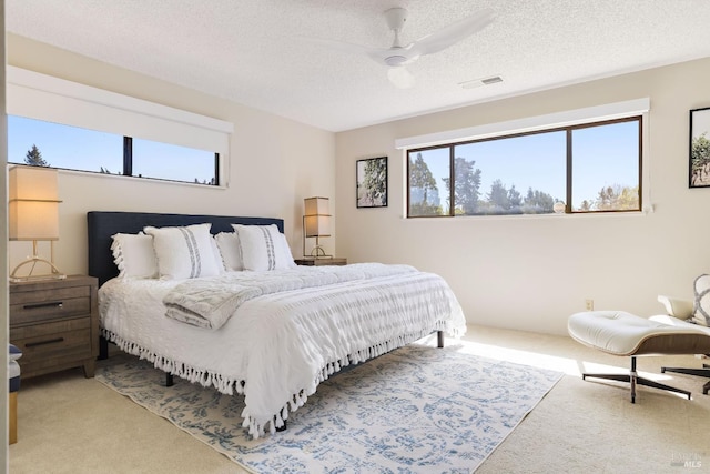 carpeted bedroom featuring visible vents, a textured ceiling, and a ceiling fan