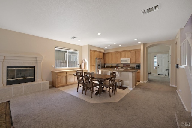 dining space featuring visible vents, arched walkways, light colored carpet, and a fireplace