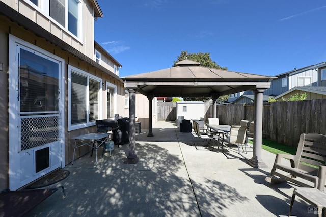 view of patio featuring outdoor dining area, a fenced backyard, an outbuilding, a gazebo, and a storage unit