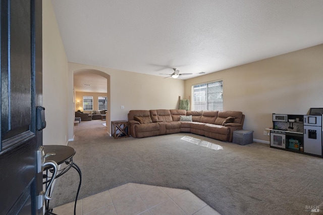 living room featuring ceiling fan, light tile patterned floors, arched walkways, light colored carpet, and baseboards