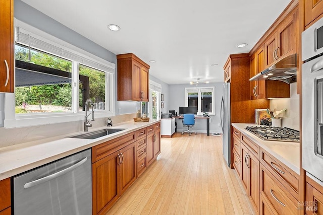kitchen with brown cabinetry, appliances with stainless steel finishes, a sink, and light countertops