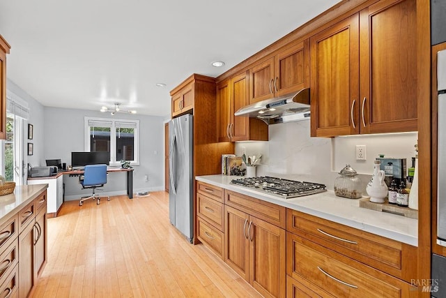 kitchen with under cabinet range hood, stainless steel appliances, light countertops, light wood-style floors, and brown cabinetry