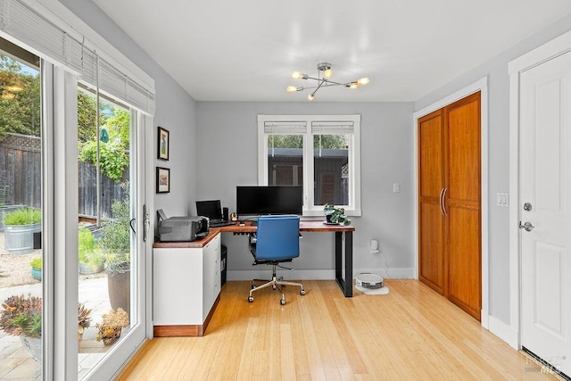 office space with a notable chandelier, baseboards, a healthy amount of sunlight, and light wood-style flooring