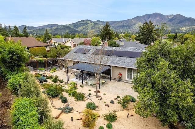 rear view of property featuring solar panels, a patio area, a shingled roof, and a mountain view