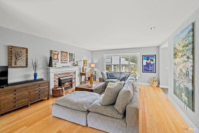 living room with baseboards, a brick fireplace, and wood finished floors