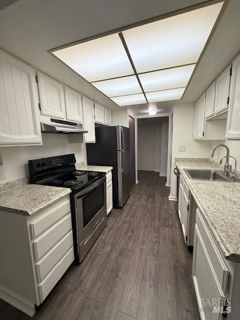 kitchen with dark wood-style flooring, white cabinets, under cabinet range hood, appliances with stainless steel finishes, and a sink