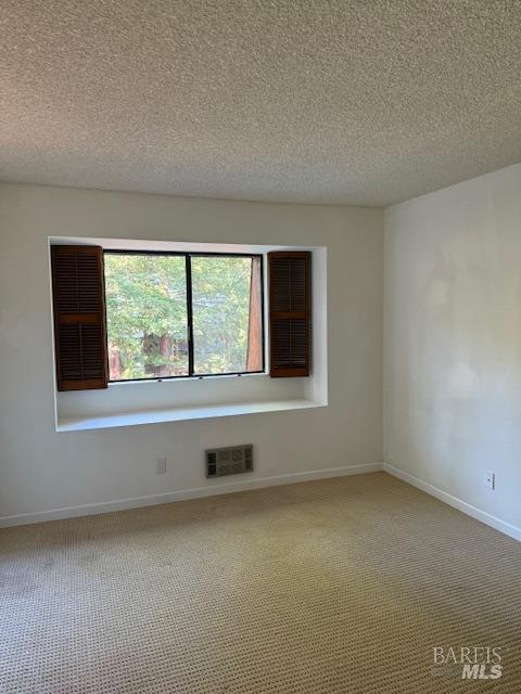 empty room featuring light carpet, visible vents, a textured ceiling, and baseboards