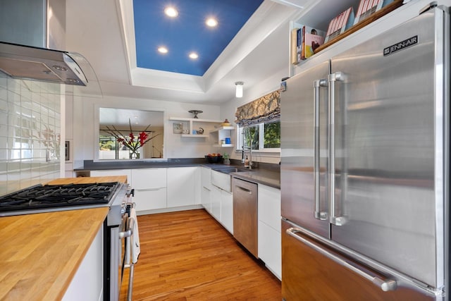 kitchen with open shelves, butcher block countertops, light wood-style floors, range hood, and stainless steel appliances
