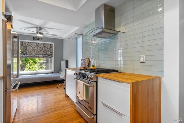 kitchen with wall chimney range hood, white cabinets, stainless steel range, butcher block countertops, and decorative backsplash