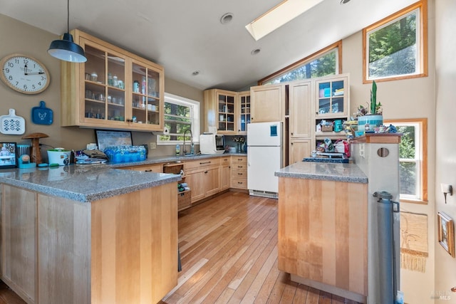 kitchen featuring vaulted ceiling with skylight, light wood-type flooring, freestanding refrigerator, a peninsula, and light brown cabinetry