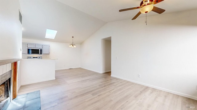 unfurnished living room with ceiling fan with notable chandelier, a fireplace, light wood finished floors, baseboards, and lofted ceiling with skylight