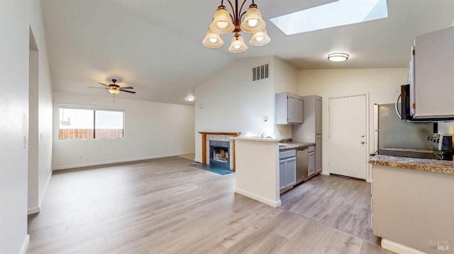 kitchen with vaulted ceiling with skylight, visible vents, gray cabinets, a tiled fireplace, and stainless steel appliances